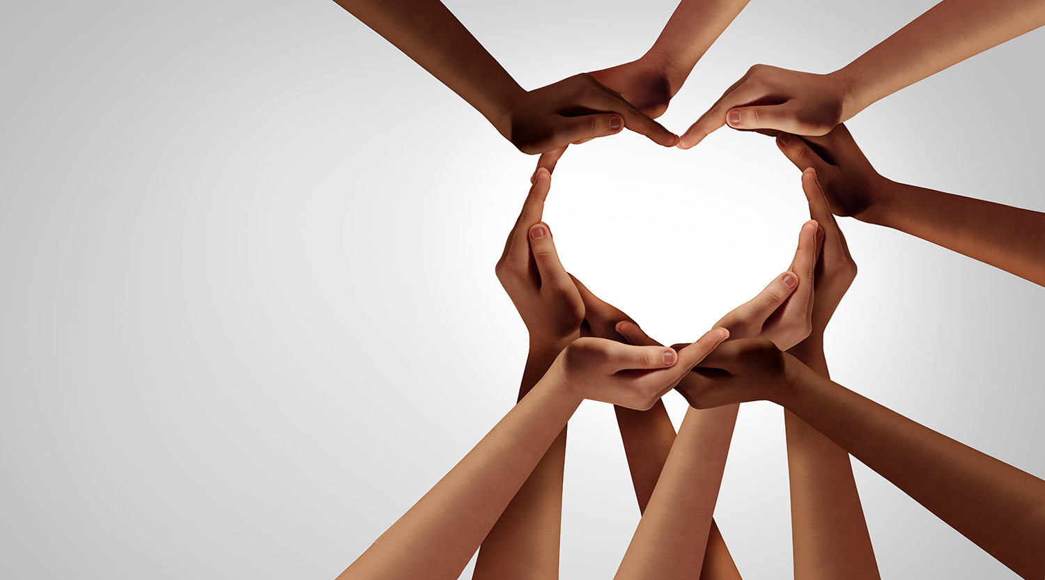A group of people hold their hands together to form a heart shape.