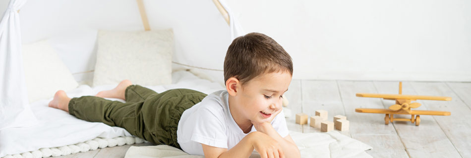 A child lies on the floor under a canvas tent in his bedroom, with a tablet in front of him