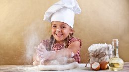 A young girl happily dusts flour over pizza dough