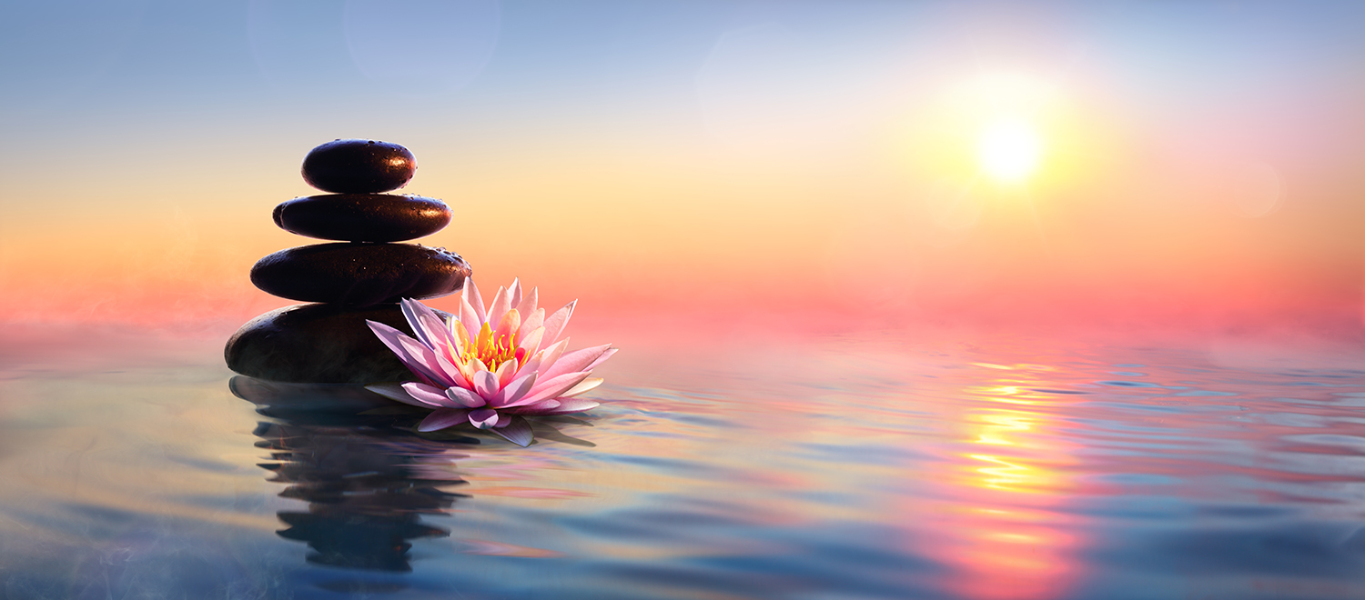 Zen stones stacked in water with a lotus to the side and a sunset in the background