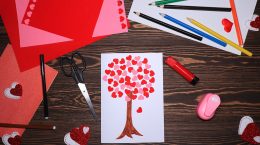 A piece of paper with a tree drawn on it and paper hearts for the leaves. In the background are craft supplies such as coloured paper, pencil crayons, scissors, and a heart punch.